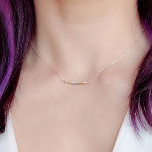 May include: A silver chain necklace with a delicate bar pendant made of alternating silver and gold beads.