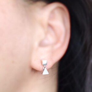 May include: A pair of silver earrings with a small square charm and a dangling triangle charm.