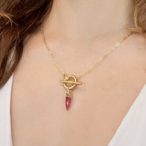 May include: A gold chain necklace with a toggle clasp and a pink gemstone pendant.