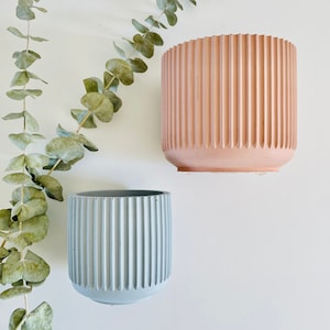 May include: Two concrete planters with a ribbed design. One planter is light blue and the other is light pink.