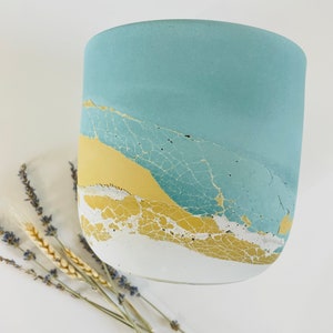 May include: A light blue, yellow, and white concrete planter with a crackled finish. The planter is round and has a wide opening.