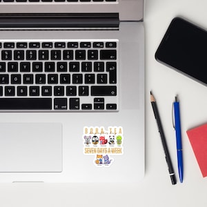 May include: A sticker featuring the text "Boba Tea" in gold letters, with cartoon animal characters holding boba tea cups. The text "Seven Days a Week" is below the characters. The sticker is on a laptop.