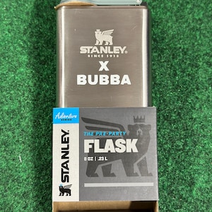 May include: A stainless steel flask with a gray cap and the text "STANLEY X BUBBA" printed on the front. The flask is accompanied by a box that reads "THE PRE-PARTY FLASK" and "8 OZ | .23 L".