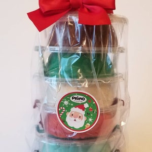 Op de afbeelding: Een stapel van vijf bakjes met klei, verpakt in doorzichtig plastic met een rode strik. De bakjes zijn in een piramidevorm gestapeld. De klei is in de kleuren bruin, groen, wit, rood en groen. De bakjes hebben een etiket met een cartoon kerstman. Het etiket zegt "Primo Playdough". De tekst "9 ounces" staat op een wit etiket bovenaan de afbeelding.