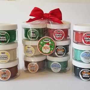 Op de afbeelding: Een set van 10 kleine potjes met klei, elk met een andere kerstgeur en kleur. De potjes zijn gerangschikt in een cadeauzak met een rode strik. De geuren zijn onder andere dennenboom, suikerkoekje, snoepstok, houtvuur en sneeuwwinter.