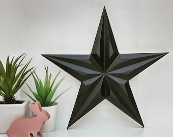 May include: A dark grey, five-pointed star with a three-dimensional design. The star is made of a textured material and has a slightly distressed look. The star is sitting on a white surface.