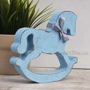 May include: A light blue wooden rocking horse with a gray and white polka dot bow. The horse is distressed and has a rustic look.