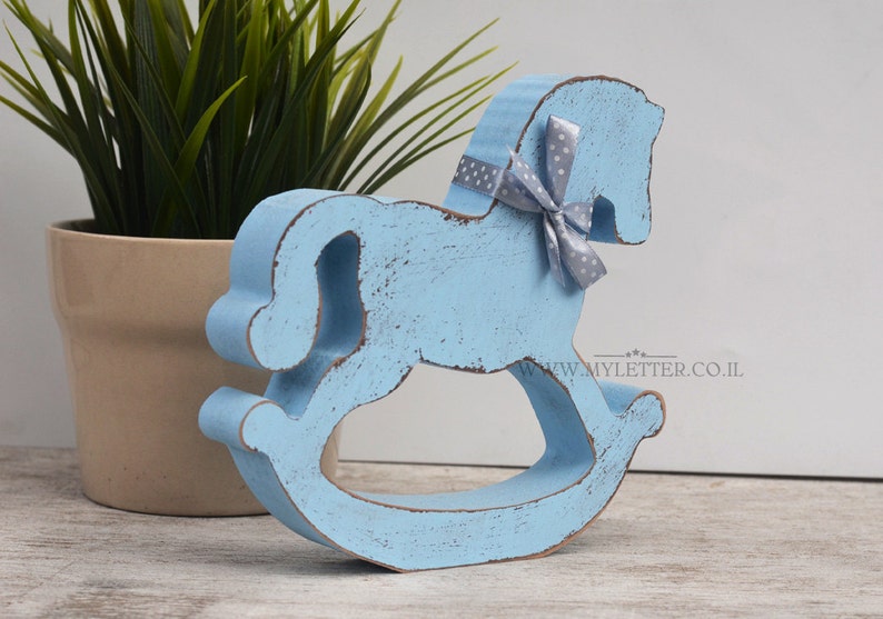 May include: A light blue wooden rocking horse with a gray and white polka dot bow. The horse is distressed and has a rustic look.