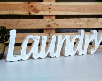 May include: White wooden sign with the word "Laundry" in a cursive font. The sign has a distressed, aged look.