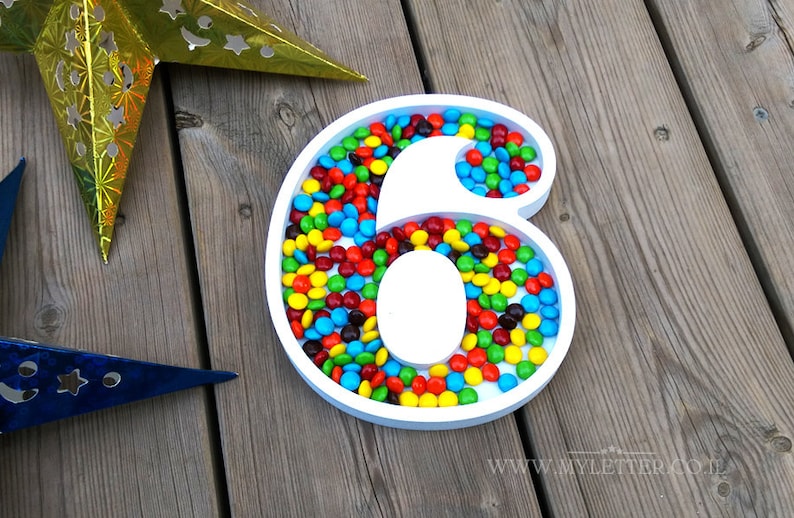 May include: A white number six shaped tray filled with colorful candy. The tray is on a wooden surface.