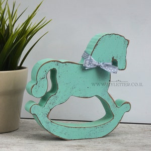 May include: A turquoise blue wooden rocking horse with a white polka dot bow. The horse is distressed and has a rustic look. The website www.myletter.co.il is printed on the base.
