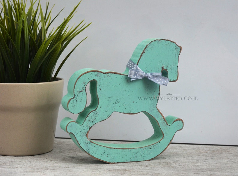 May include: A turquoise blue wooden rocking horse with a white polka dot bow. The horse is distressed and has a rustic look. The website www.myletter.co.il is printed on the base.