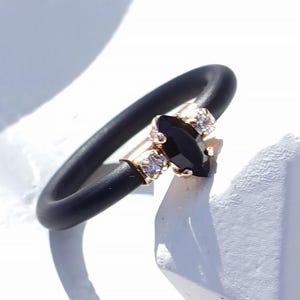Op de afbeelding: Een zwarte siliconen ring met een roségouden zetting, voorzien van een centrale zwarte steen in marquise-slijpvorm geflankeerd door twee kleine heldere steentjes. De tekst "BLACK | ROSE GOLD" staat in de rechterbenedenhoek van de afbeelding.