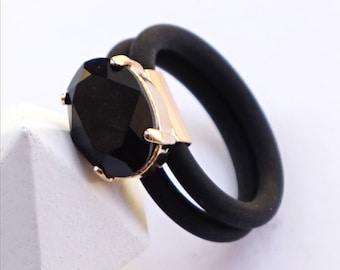 Puede incluir: Dos anillos con bandas negras mate y piedras ovaladas facetadas. El anillo superior tiene una piedra ópalo arena engastada en garras de oro amarillo brillante. El anillo inferior tiene una piedra negra engastada en oro rosa. Texto: SAND OPAL | SHINY YELLOW GOLD y BLACK | ROSE GOLD.