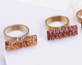 May include: Three rings with rectangular, wire-wrapped gemstone accents. The rings have matte gold bands. Gemstone colours include topaz, red opaque, and light amethyst. The text at the bottom reads: Topaz Matte Gold, Red Opaque Matte Gold, and Light Amethyst Rose Gold.