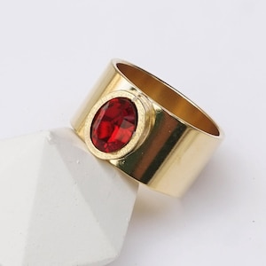May include: A gold ring with a red oval gemstone. The ring has a shiny gold finish.