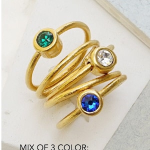 Puede incluir: Conjunto de anillos de oro con cinco bandas y piedras preciosas de colores. Las piedras preciosas son topacio, peridoto, rosa, esmeralda, cristal y zafiro.