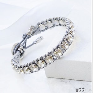 Może przedstawiać: Dwa srebrne i fioletowe bransoletki z kryształowymi ozdobami. Bransoletki są wykonane ze skóry i mają srebrną klamrę. Bransoletki są pokazane na białym tle.