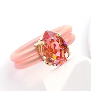 May include: A ring with a pear-shaped, iridescent gemstone set in yellow gold. The ring band is made of a pink silicone material.  ROSE PEACH | YELLOW GOLD