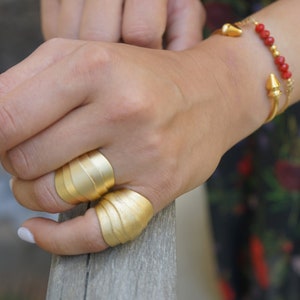 May include: Two gold rings with a wavy design. The rings are worn on the index and middle fingers of a hand.
