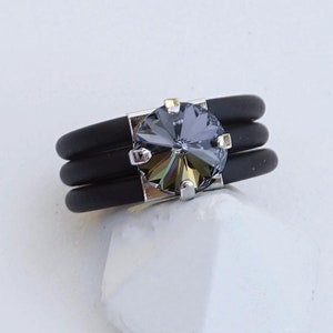 May include: A black silicone ring with a silver setting and a gray iridescent gemstone. The ring is on a white background.