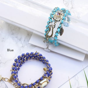 Op de afbeelding: Twee gelaagde armbanden met een gouden ketting en kristallen accenten. De armband aan de linkerkant is blauw en de armband aan de rechterkant is turquoise.