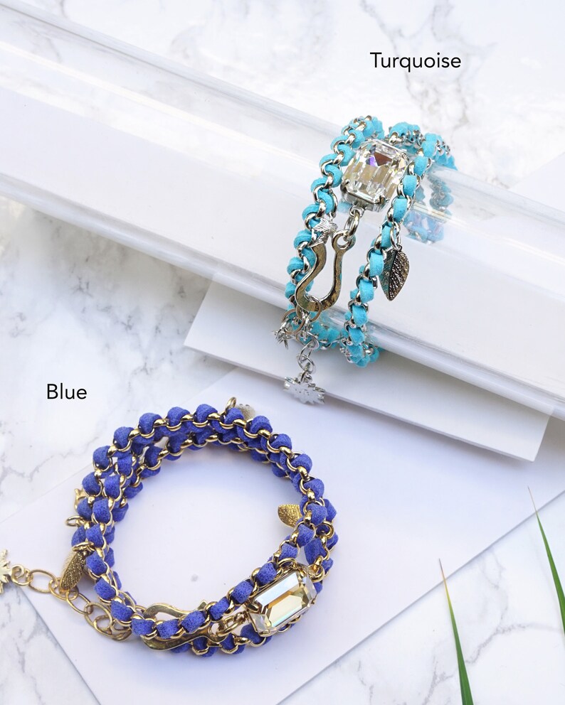 Op de afbeelding: Twee gelaagde armbanden met een gouden ketting en kristallen accenten. De armband aan de linkerkant is blauw en de armband aan de rechterkant is turquoise.
