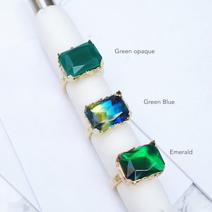 K&ouml;nnte beinhalten: Drei goldene Ringe mit verschiedenen farbigen Steinen. Der obere Ring hat einen undurchsichtigen gr&uuml;nen Stein, der mittlere Ring hat einen gr&uuml;n-blauen Stein und der untere Ring hat einen dunkelgr&uuml;nen Stein. Die Ringe sind mit "Gr&uuml;n undurchsichtig", "Gr&uuml;n Blau" und "Smaragd" beschriftet.