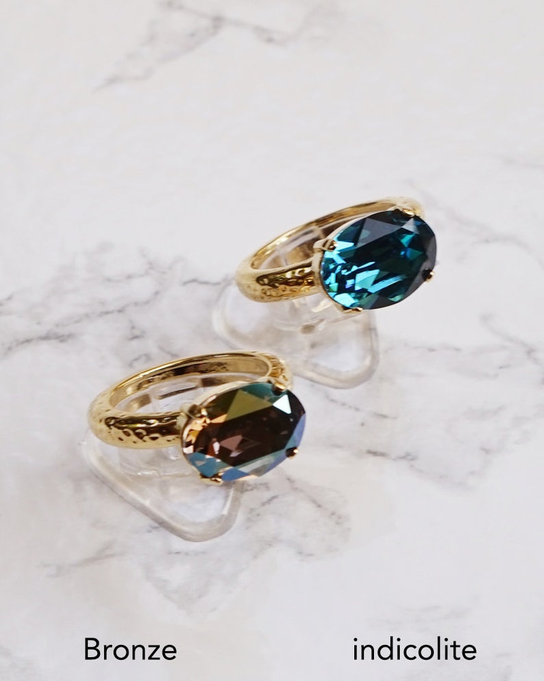 May include: Two rings with gold-toned hammered bands and oval-cut faceted stones. One ring features a deep blue indicolite stone, while the other displays a metallic bronze stone. The text Bronze and indicolite appears at the bottom.