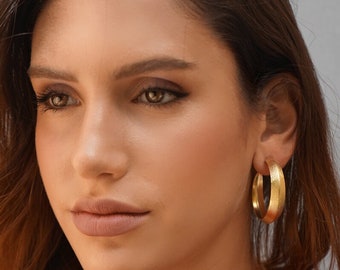 May include: A pair of gold hoop earrings with a textured finish. The earrings are large and have a slightly oval shape.