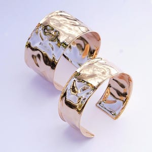Könnte beinhalten: Zwei gehämmerte goldfarbene Metallarmbänder. Das größere Armband ist breiter als das kleinere Armband. ROSE GOLD ist unten im Bild in weißer Schrift geschrieben.