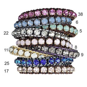 Pode incluir: Um conjunto de oito pulseiras coloridas com enfeites de cristal. As pulseiras são feitas de couro e apresentam diferentes cores de cristais, incluindo rosa, azul, branco e preto. As pulseiras são numeradas 38, 6, 5, 8, 9, 22, 25 e 17.