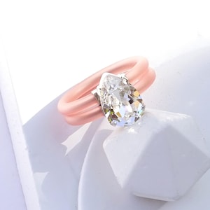 May include: A pink silicone ring with a clear pear-shaped crystal. The ring is double-banded and has a silver setting for the crystal. CLEAR | SILVER