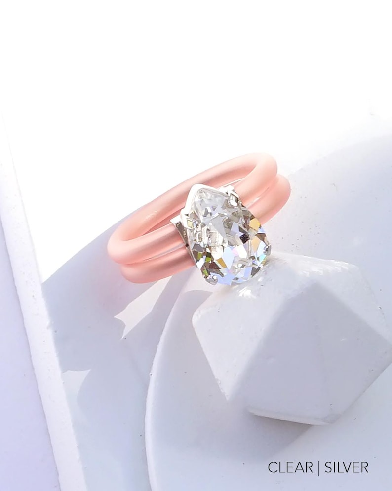 May include: A pink silicone ring with a clear pear-shaped crystal. The ring is double-banded and has a silver setting for the crystal. CLEAR | SILVER