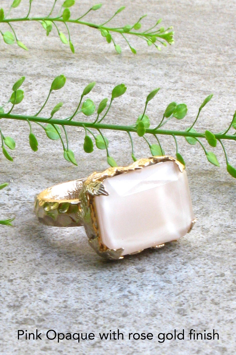 May include: A ring with a large, rectangular, opaque pink stone set in a gold setting with leaf-like details. The ring has a rose gold finish.