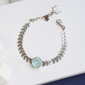 Puede incluir: Una pulsera de tono plateado con una cadena de eslabones en forma de chevr&oacute;n y una piedra cuadrada de color azul claro texturizada. La pulsera incluye un cierre de mosquet&oacute;n, un dije de coraz&oacute;n y un dije de estrella con el texto Lagoon.