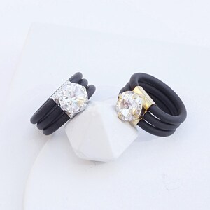 May include: Two black silicone rings with a clear rhinestone in the center. The ring on the left has a silver setting, and the ring on the right has a yellow gold setting. CLEAR SILVER | CLEAR YELLOW GOLD.