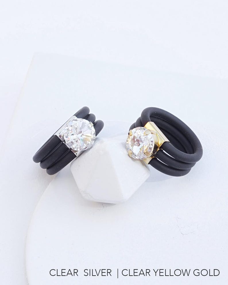 May include: Two black silicone rings with a clear rhinestone in the center. The ring on the left has a silver setting, and the ring on the right has a yellow gold setting. CLEAR SILVER | CLEAR YELLOW GOLD.