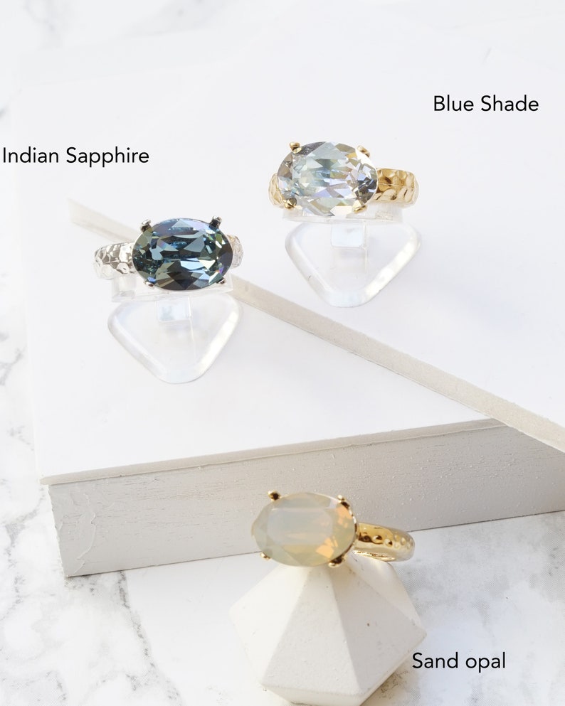 May include: Three rings with oval-shaped stones and textured bands. One ring features an Indian Sapphire stone on a silver-toned band, another has a Blue Shade stone on a gold-toned band, and the third has a Sand Opal stone on a gold-toned band.