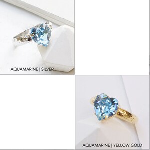 May include: Two rings featuring a heart-shaped light blue aquamarine crystal. One ring has a silver band with a hammered texture, and the other has a yellow gold band with a hammered texture. The text AQUAMARINE | SILVER and AQUAMARINE | YELLOW GOLD appears.