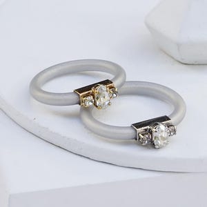 May include: Two silver rings with a clear stone and smaller clear stones on each ring. The ring on the bottom has a silver band and the ring on top has a gold band.  SILVER SHADE | GOLD/SILVER