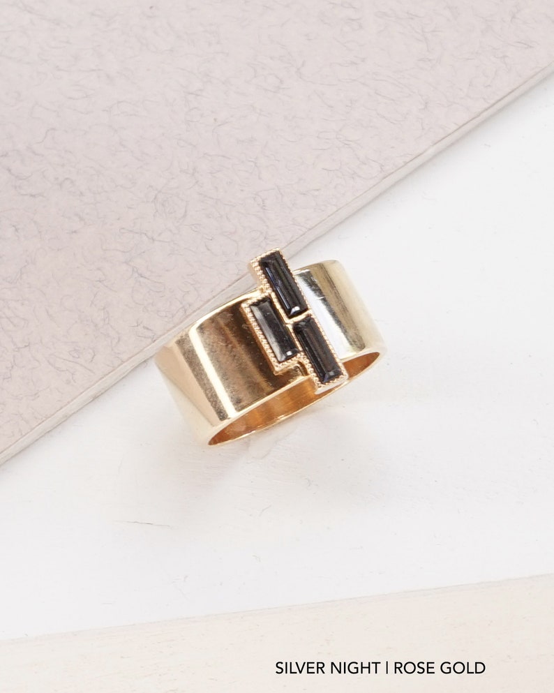 Puede incluir: Un anillo de oro rosa con un dise&ntilde;o geom&eacute;trico negro. El anillo est&aacute; sobre una superficie blanca. SILVER NIGHT | ROSE GOLD