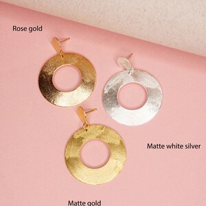 May include: Three pairs of hoop earrings in rose gold, matte gold, and matte white silver. The earrings are all the same size and shape, with a hammered texture.