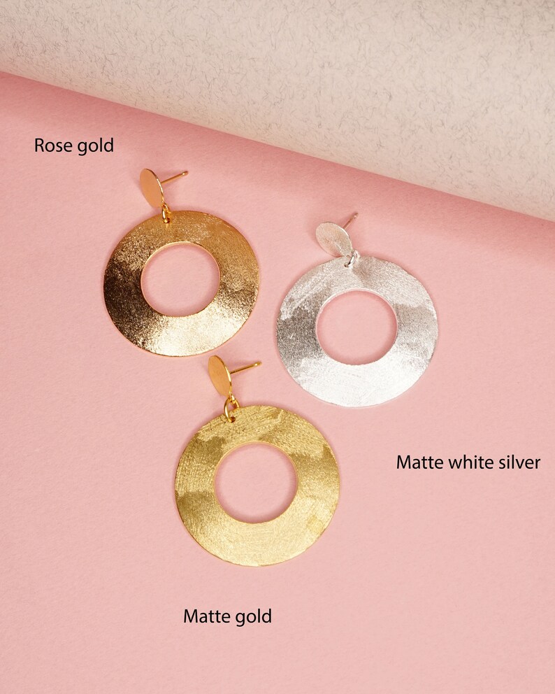May include: Three pairs of hoop earrings in rose gold, matte gold, and matte white silver. The earrings are all the same size and shape, with a hammered texture.