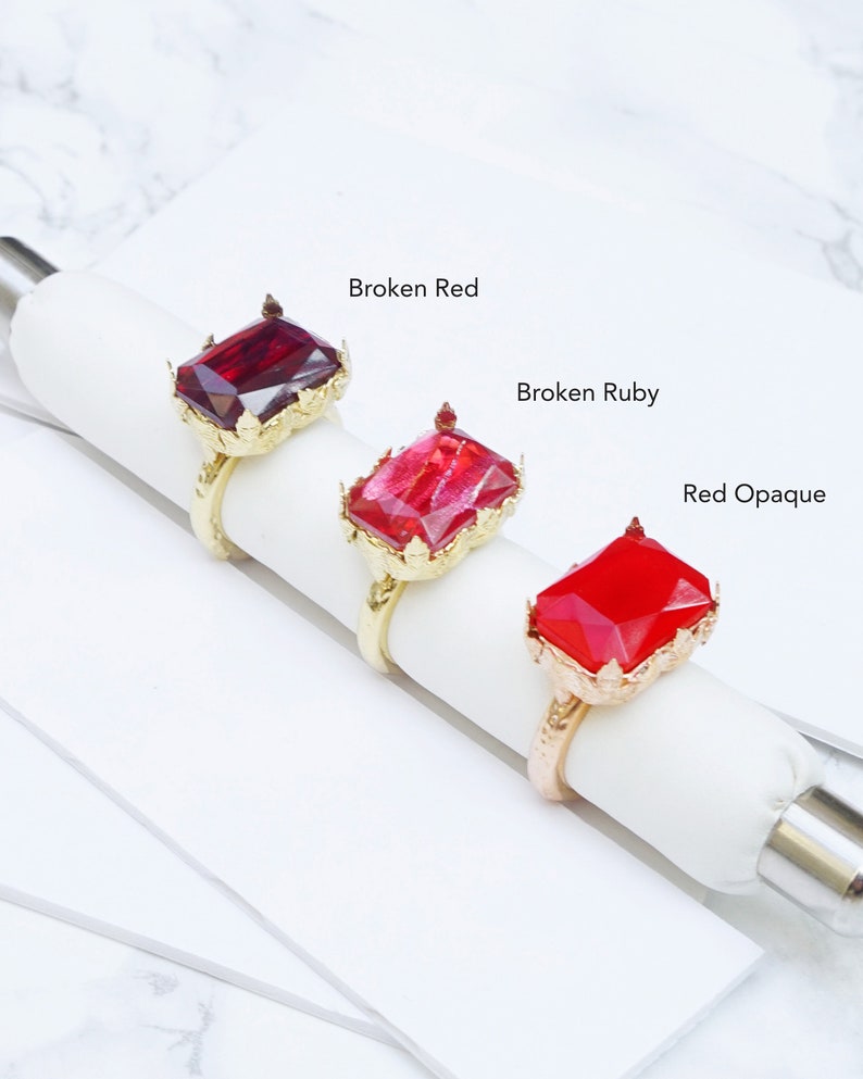 K&ouml;nnte beinhalten: Drei goldene Ringe mit verschiedenen roten Edelsteineins&auml;tzen. Die Ringe sind mit "Broken Red", "Broken Ruby" und "Red Opaque" beschriftet.