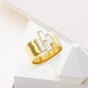 Puede incluir: Un anillo de oro con acabado mate y tres cristales transparentes en forma de baguette engastados en la banda. CLEAR CRYSTAL | MATTE GOLD