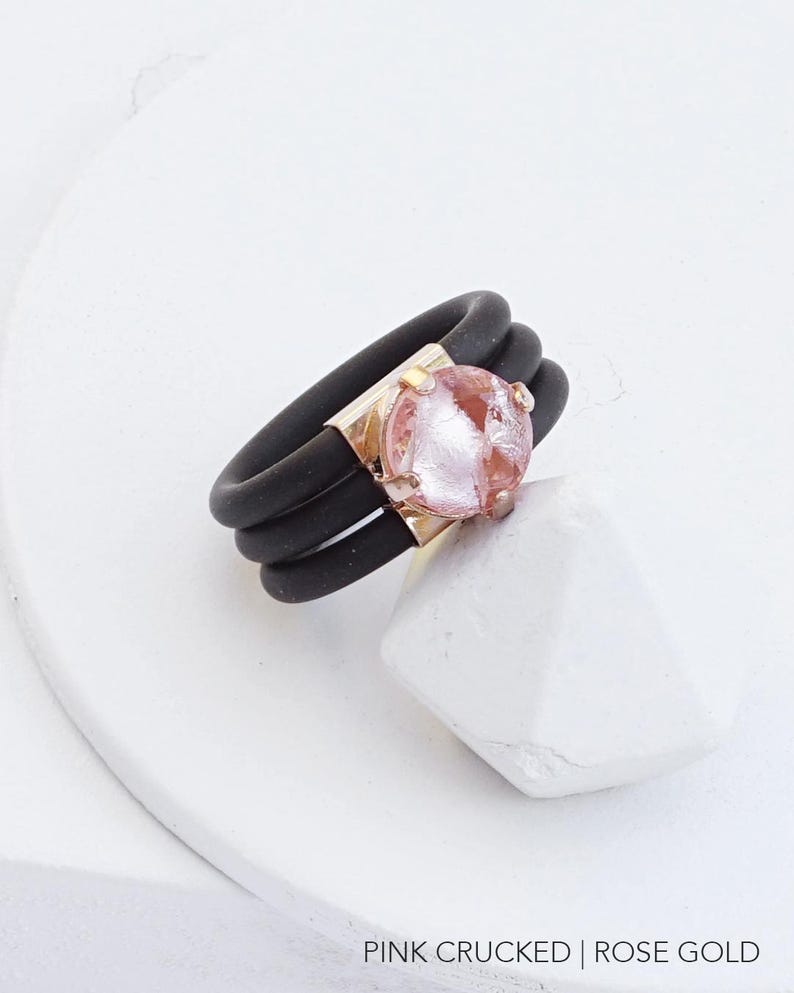 May include: A black silicone ring with three bands and a rose gold setting with a pink cracked glass stone.