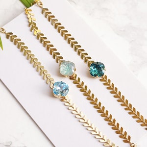 Puede incluir: Tres pulseras doradas con un dise&ntilde;o de cadena en patr&oacute;n de espiga. Cada pulsera tiene un cristal facetado central en diferentes tonos: azul aguamarina claro, azul laguna p&aacute;lido y azul cerceta indicolita, seg&uacute;n se indica en la imagen.