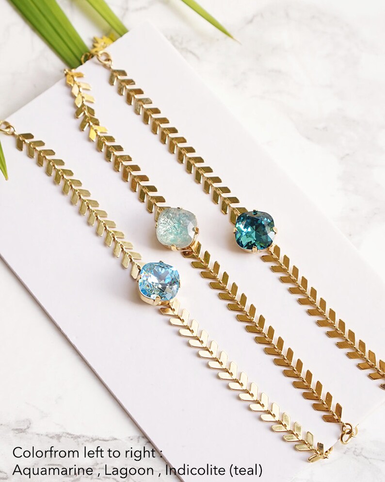 Puede incluir: Tres pulseras doradas con un dise&ntilde;o de cadena en patr&oacute;n de espiga. Cada pulsera tiene un cristal facetado central en diferentes tonos: azul aguamarina claro, azul laguna p&aacute;lido y azul cerceta indicolita, seg&uacute;n se indica en la imagen.
