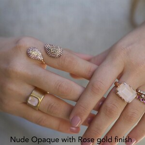 May include: A set of four rings with rose gold finish. The rings feature a variety of stones, including a large rectangular pink stone, smaller pink stones, and clear stones. The text "Nude Opaque with Rose gold finish" is visible at the bottom of the image.